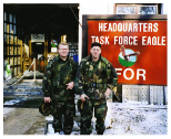 Image of 2 soldiers posing for a photo in front of the Headquarters for Task Force Eagle.